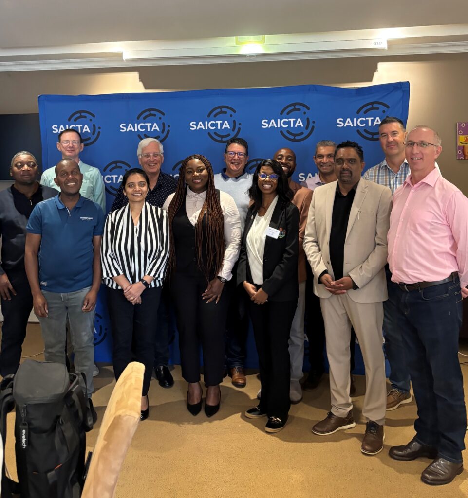 Group of diverse professionals posing for a photo in front of a blue SAICTA backdrop with logos.